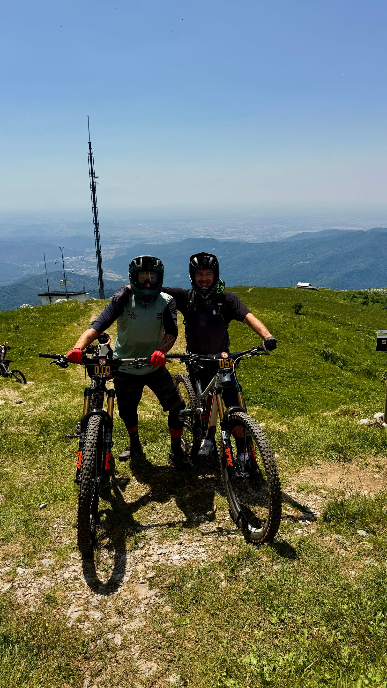 Filip standing with an enduro bike on the grassy Mount Matajur summit.
