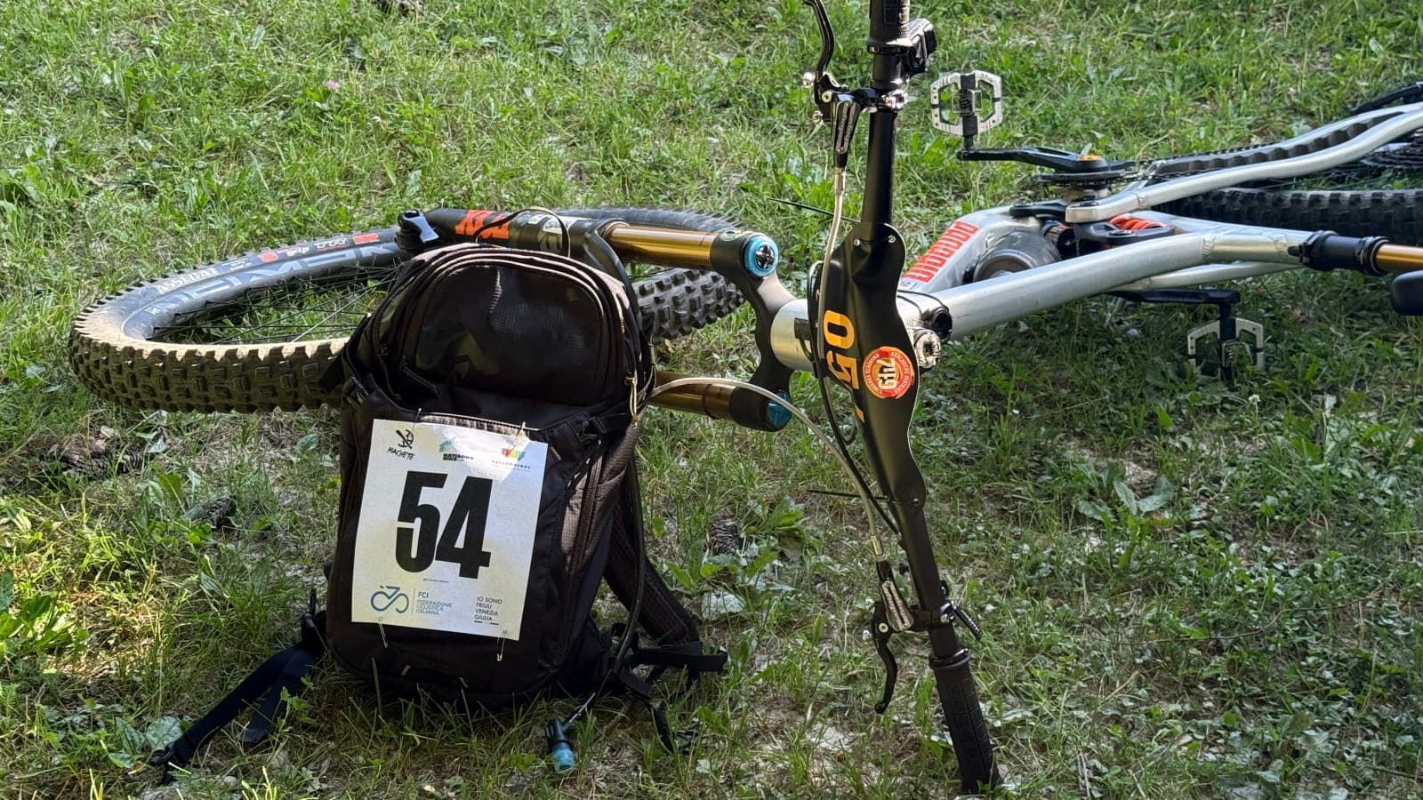 Enduro bike with race number 54 lying on the grass after rear hub repair work.