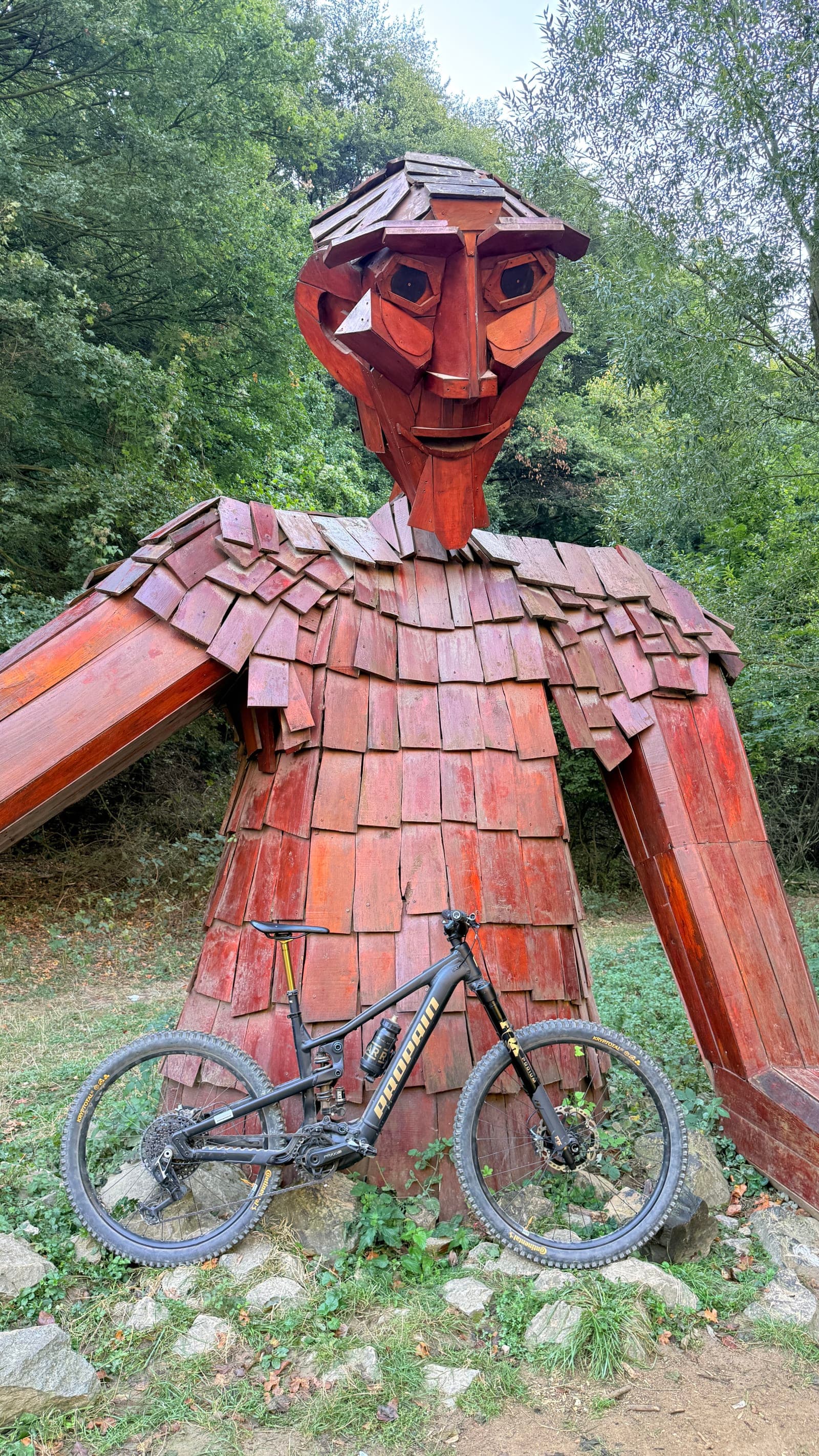 A mountain bike leaning against a giant red wooden figure sculpture in the Mecsek hills near Pécs, Hungary.